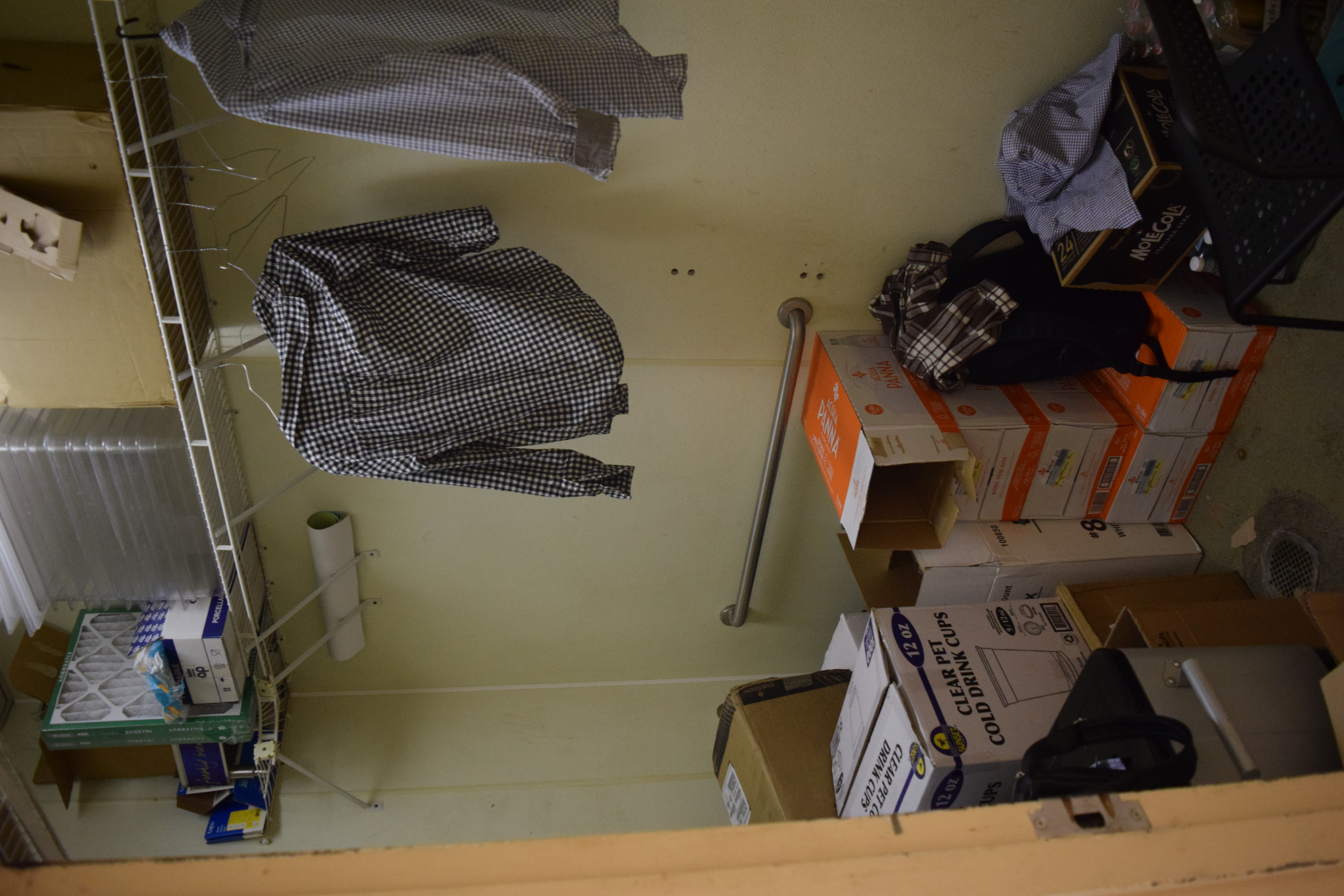Personal clothing stored on hangers next to dry goods and disposables — hygiene and brand-policy violation