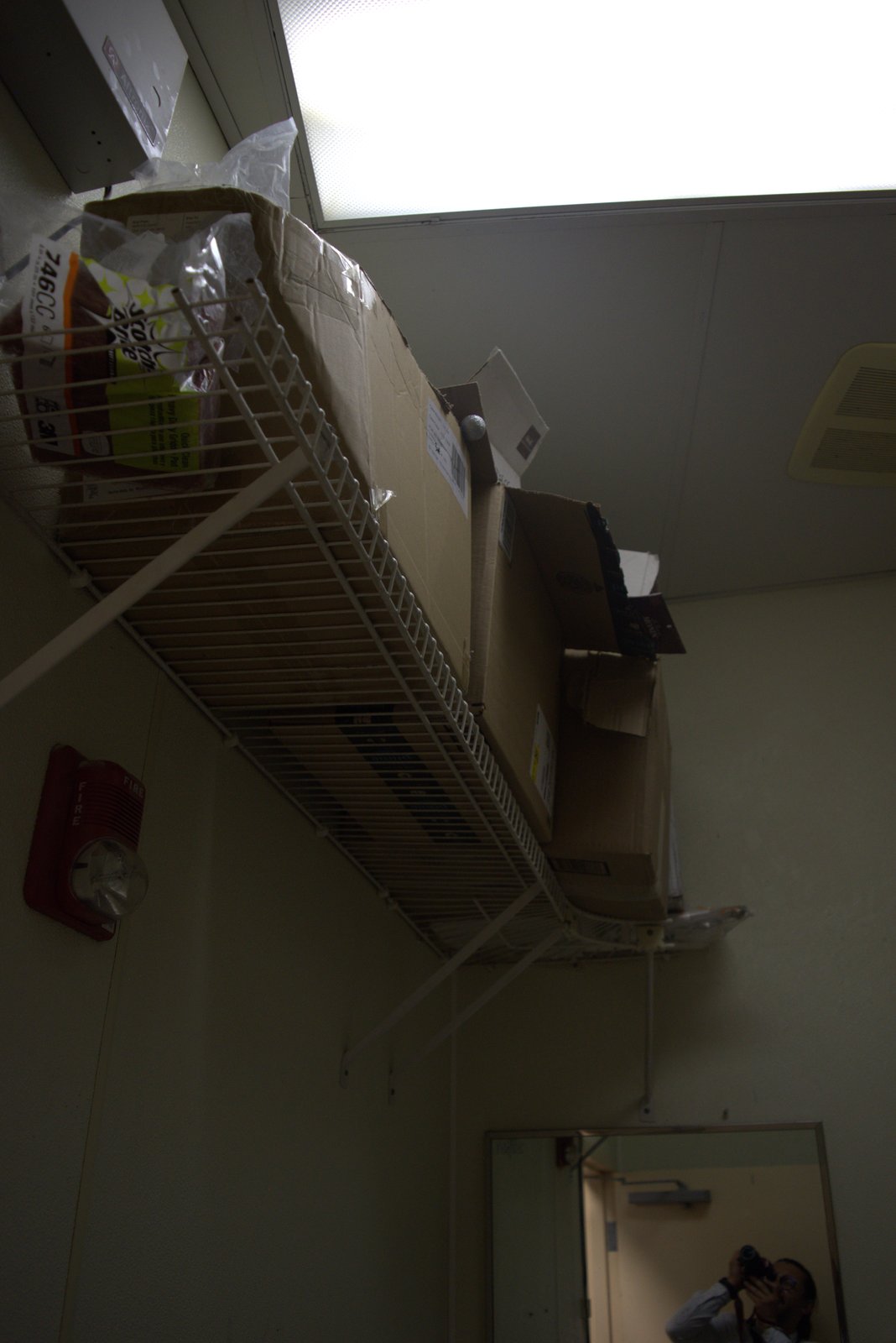 Overhead storage shelf — torn, overstuffed boxes spilling above the fire alarm and ceiling tiles