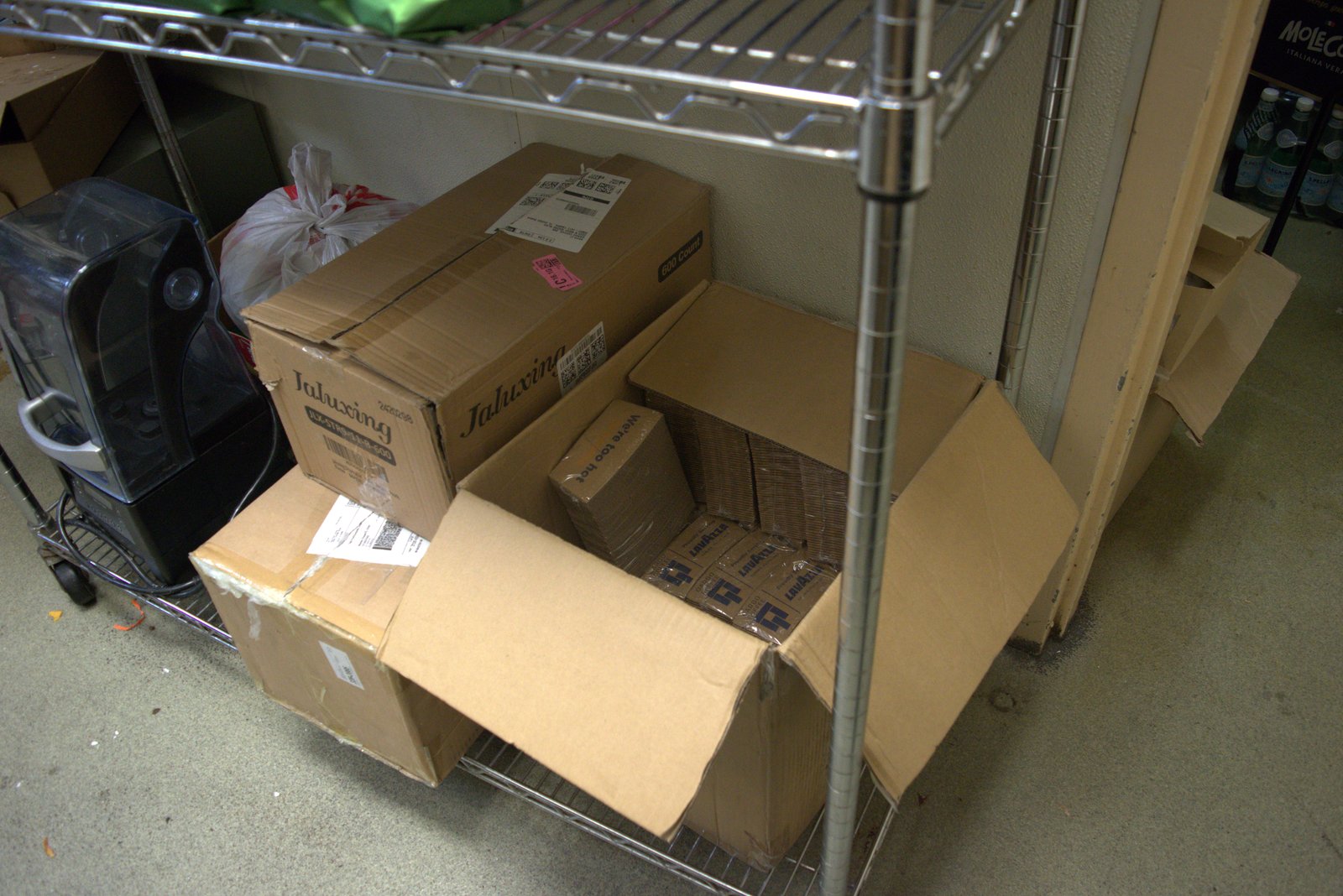 Loose, unauthorized inventory (Lavazza espresso, Jaluxing boxes) stored directly on wire shelving next to Mole Cola crates