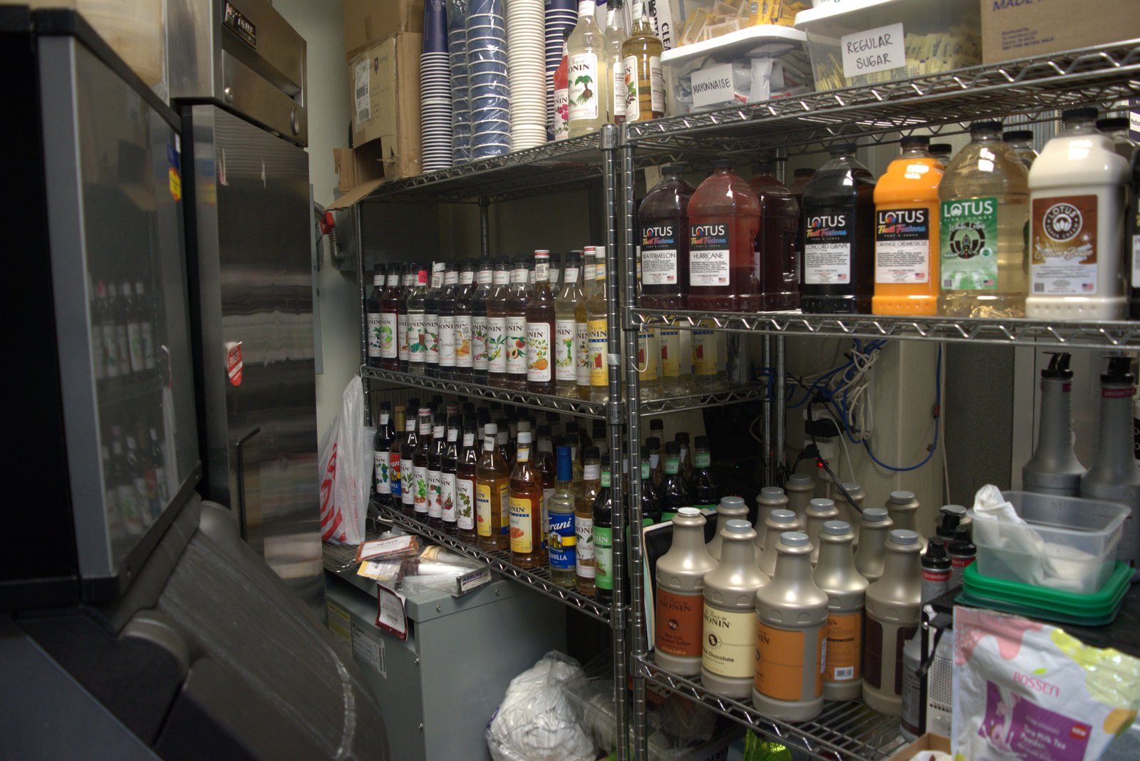 Rows of unapproved Monin and Lotus bottles dominating storage instead of Qargo-spec product