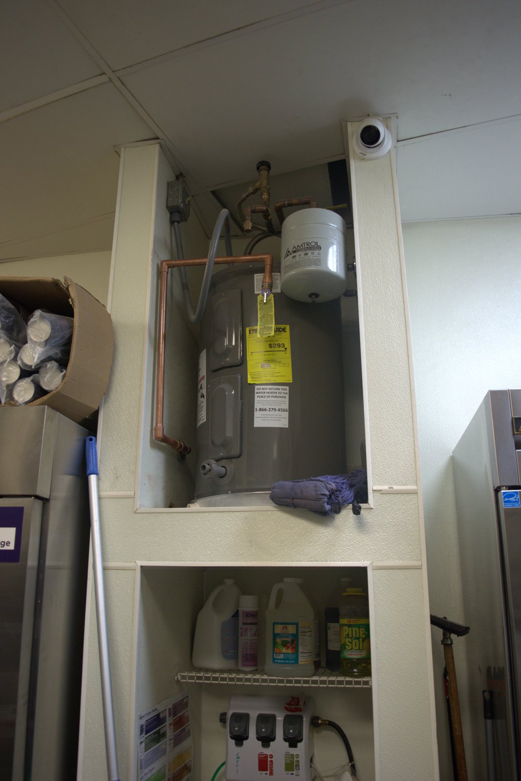 Water-heater alcove and chemical closet — soiled mop draped on top of the water heater; cardboard storage stacked next to it