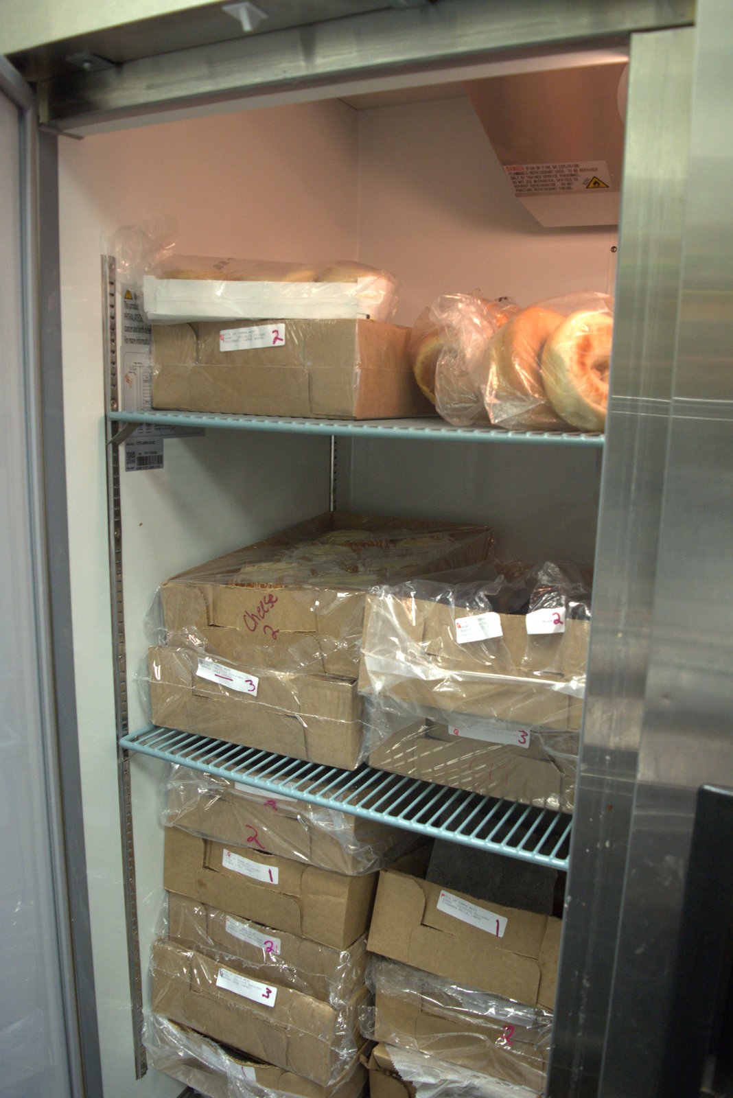 Walk-in fridge — bakery boxes stored directly on shelving with no individual product expiration labeling