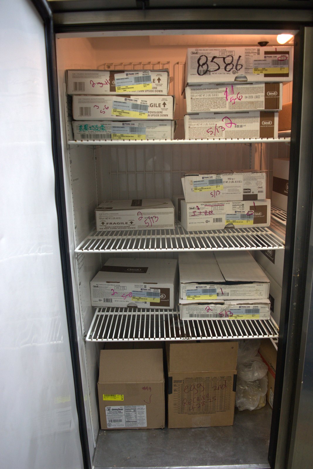 Same freezer, wider — multiple cases dated 5/13 and 5/6 stacked above 'egg 2nd Receive 4/28/25' carton; no clear FIFO rotation system in place