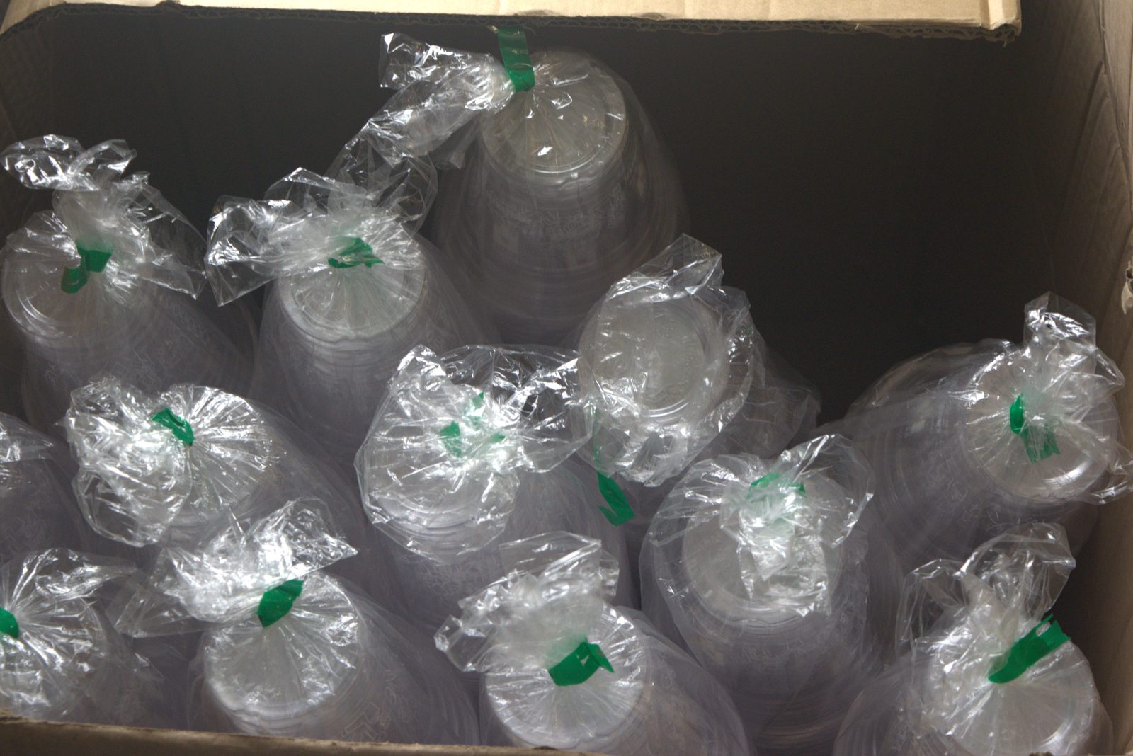 Inside one of the overhead boxes — dozens of unbranded clear cup sleeves loosely tied with green plastic ties, stored in a torn shipping carton instead of approved sealed packaging