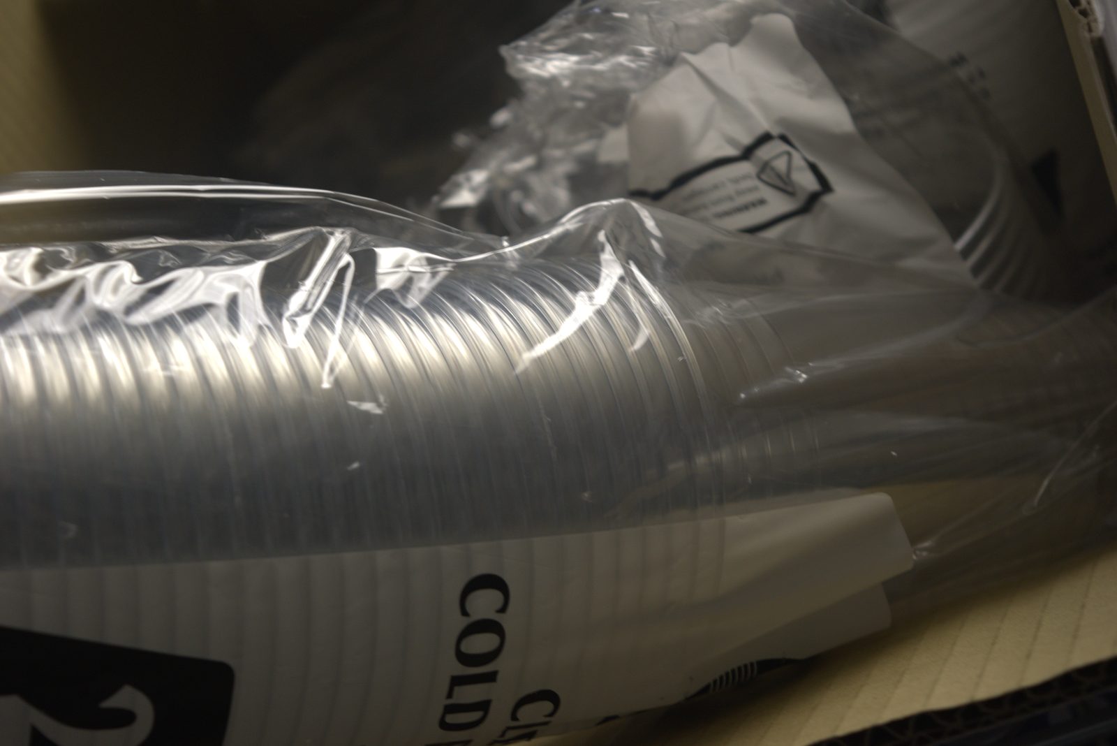 Detail of an unbranded 'CLEAR COLD' cup sleeve — generic, non-Qargo packaging stored loosely in a cardboard box on overhead shelving