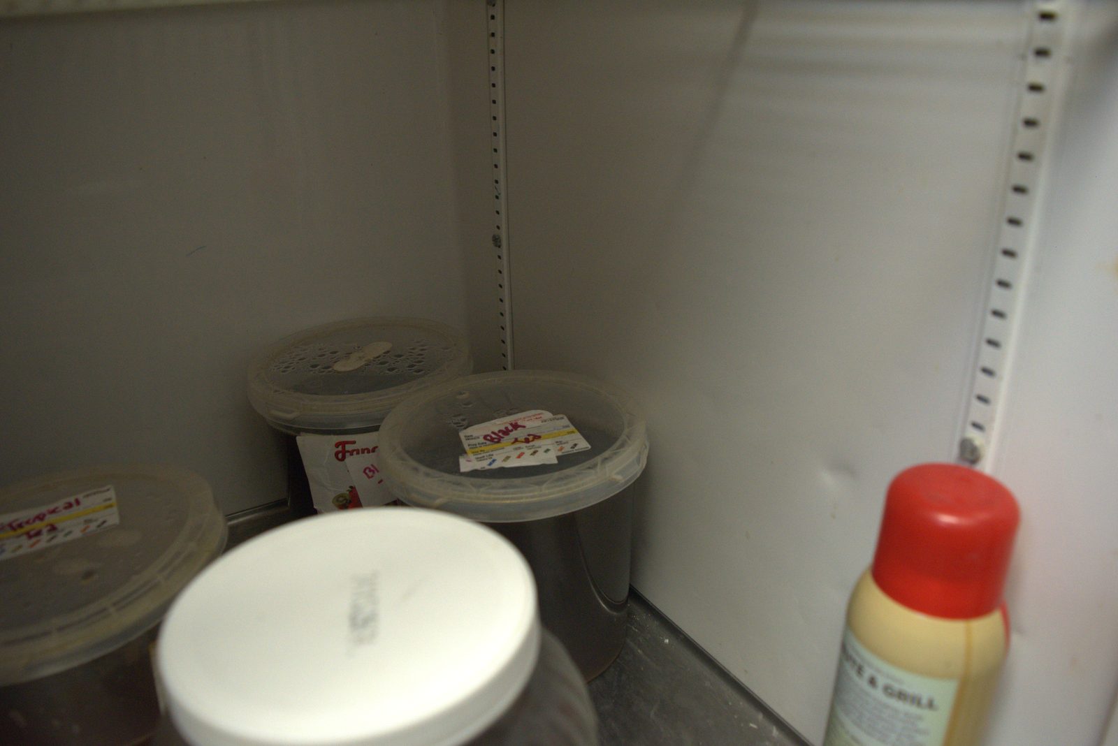 Multiple unlabeled tubs of brown syrup/liquid stacked on the fridge floor next to a retail-grade marinade bottle