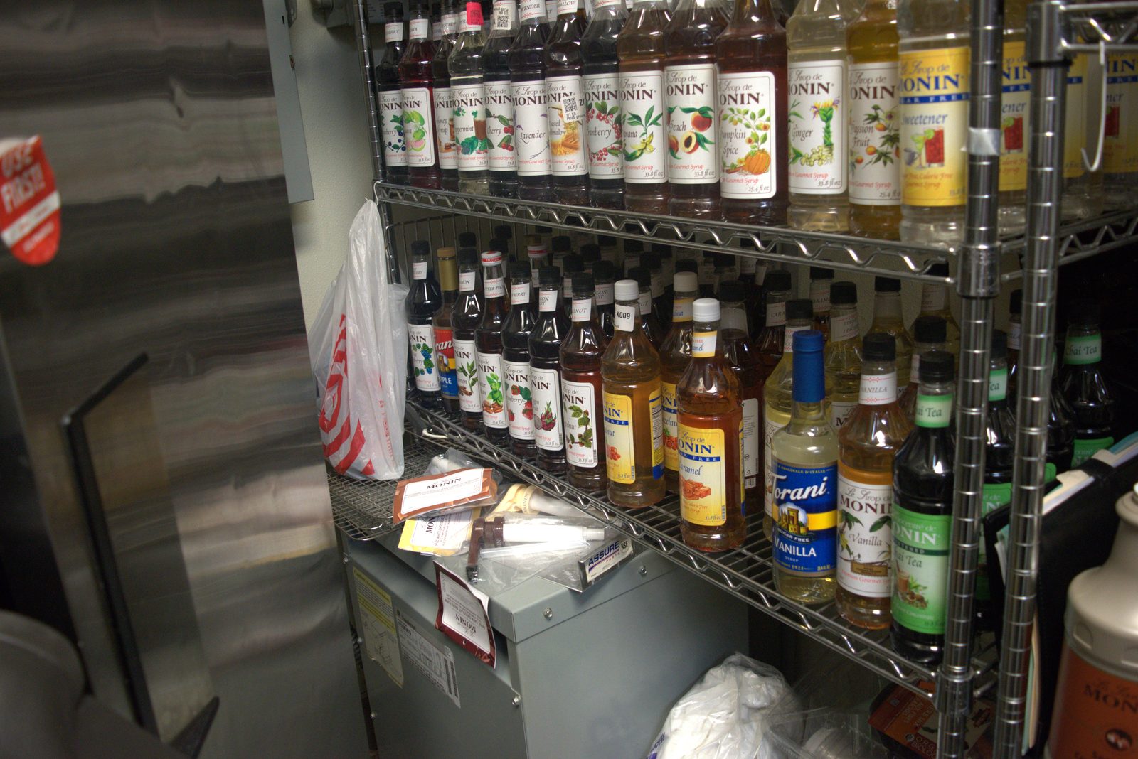 Syrup wall — entire shelving unit stocked with unauthorized Monin and Torani retail-grade syrups instead of the Qargo line
