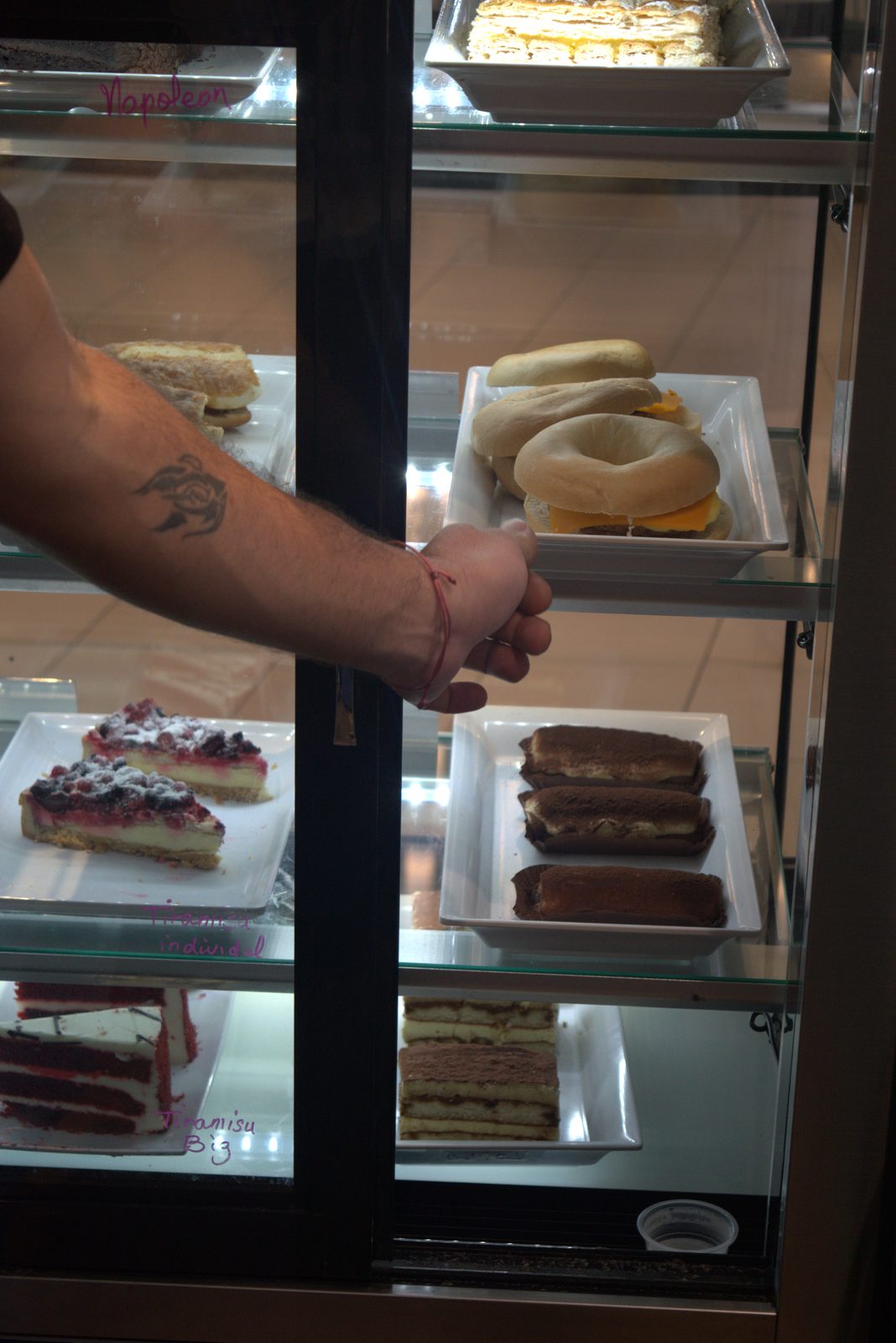Front-of-house pastry case — staff member reaching directly into the open display case with a bare arm (no glove, no utensil)