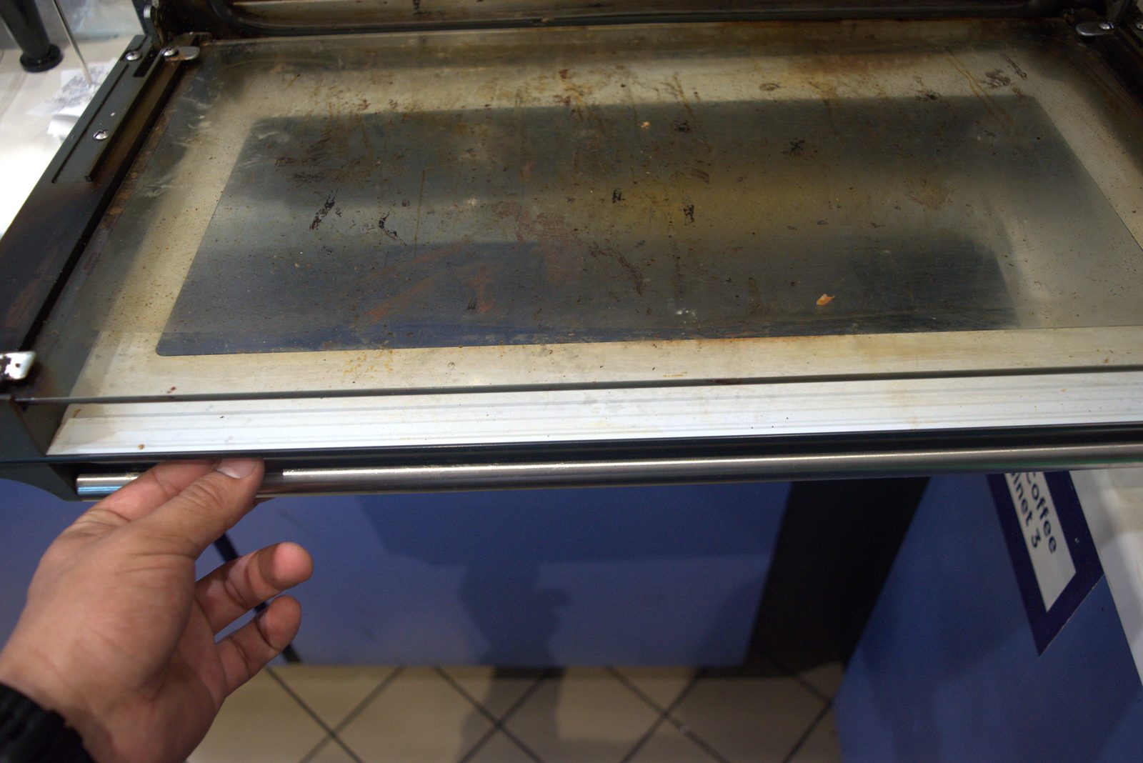 Pastry-case interior glass shelf — heavy rust streaks, food debris and grime across the food-contact surface