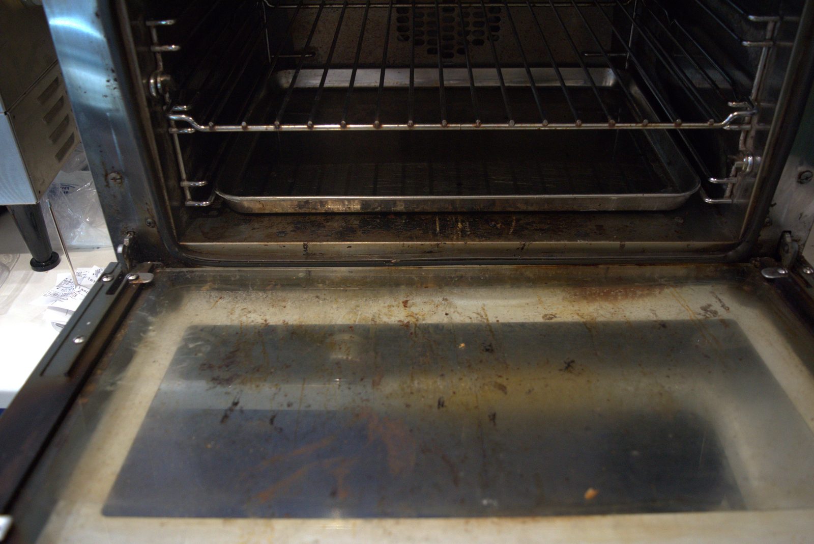 Convection oven door — interior glass coated with baked-on grease and food splatter; door gasket area heavily soiled