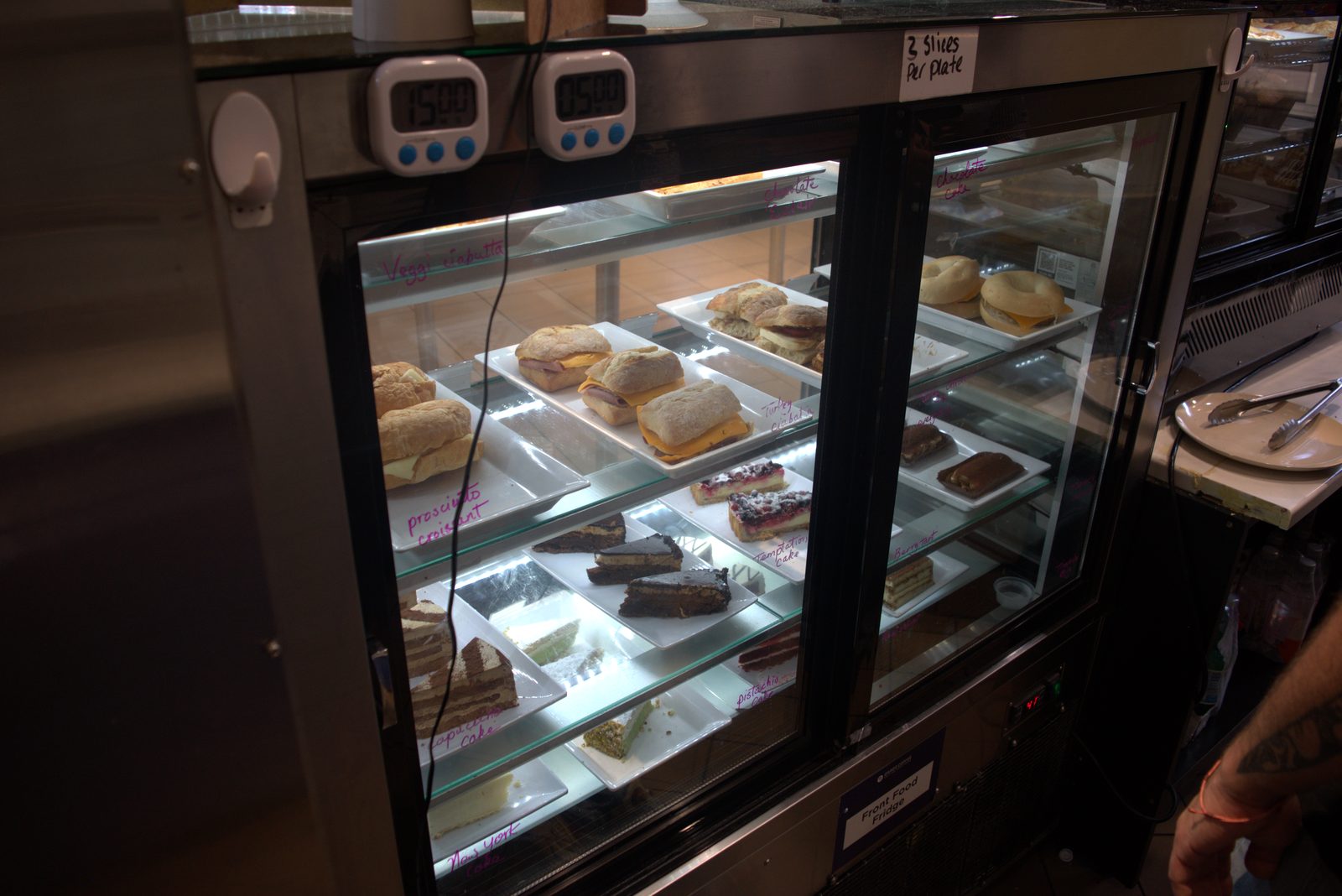 Front Food Fridge — products labeled in handwritten pink marker directly on the glass; consumer kitchen timers stuck on top