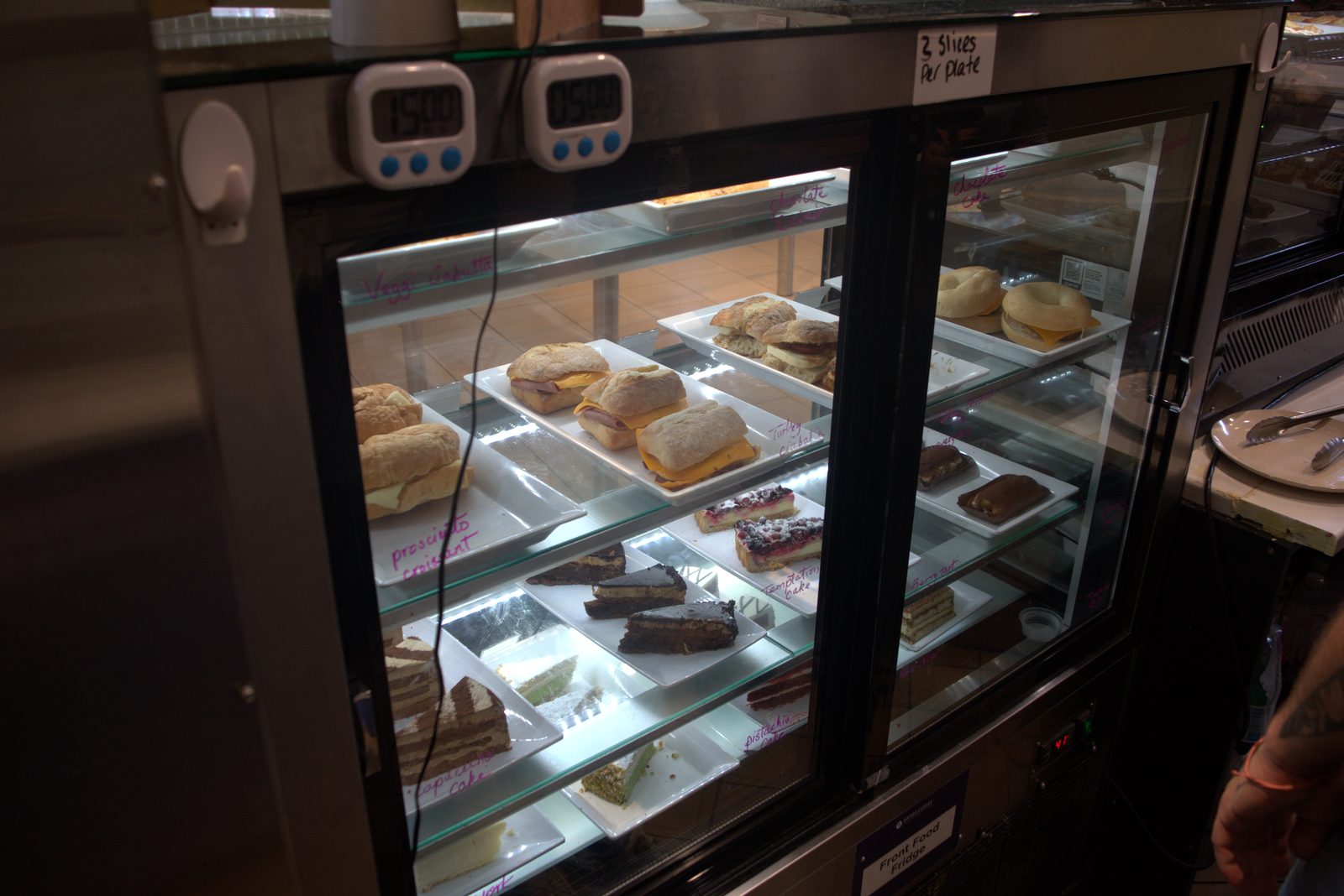 Same Front Food Fridge, alternate angle — confirms heavy use of marker-on-glass labeling, ham-and-cheese ciabatta sandwiches and assorted cakes displayed without printed allergen/ingredient cards required by Qargo brand standard