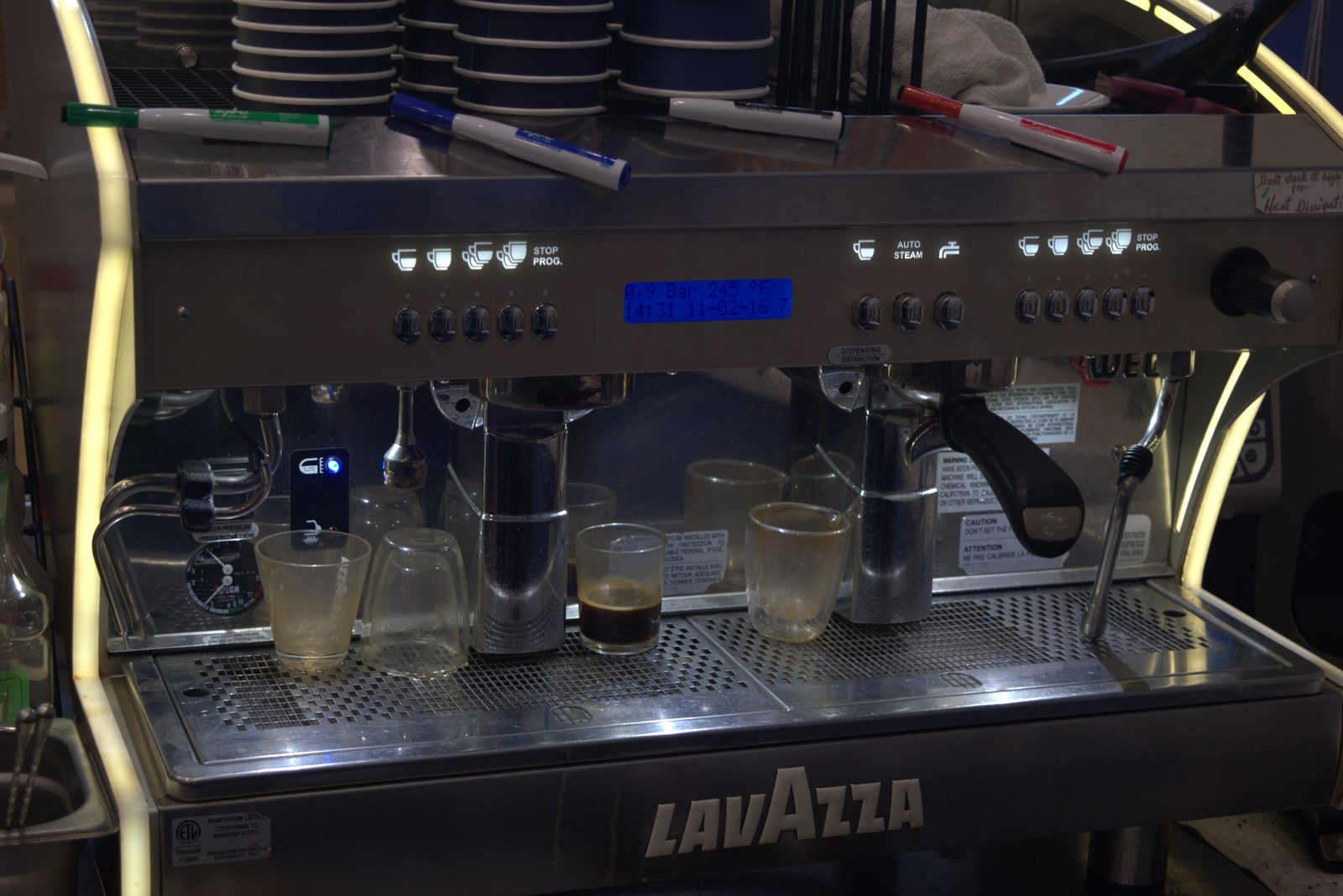 Active service espresso machine is a Lavazza two-group unit; used shot glasses on the drip tray and markers on the cup warmer