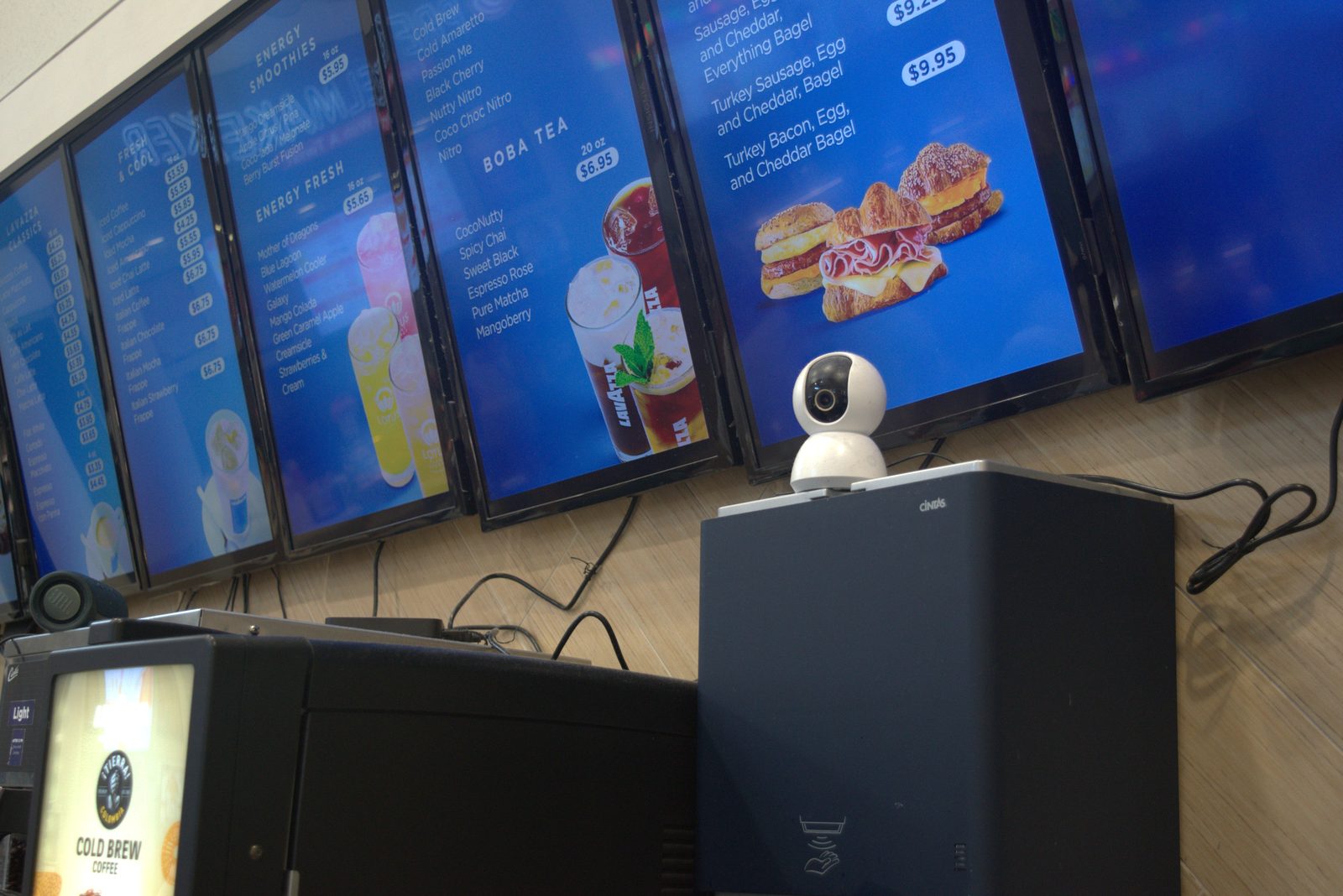 Customer-facing menu boards use Lavazza-branded boba tea imagery; consumer Wi-Fi webcam instead of the required Solink camera