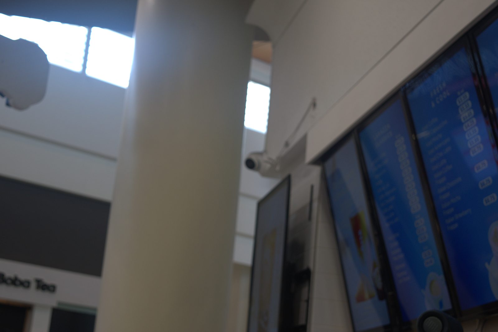 Mall ceiling above the storefront — a wall-mounted bullet security camera is aimed at the Qargo Coffee menu boards and counter; this is mall-property surveillance, not the franchisor-required Solink in-store system